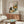 May include: Framed poster print displayed above walnut credenza in modern living room with white curved chair and glass coffee table. Artwork shows black cat sitting at checkered tablecloth table with yellow coffee cup and colorful flower bouquet including sunflowers, pink blooms in green vase. Print has warm beige background with natural lighting creating window shadows across scene.