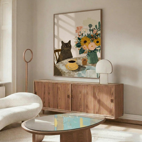 May include: Framed poster print displayed above walnut credenza in modern living room with white curved chair and glass coffee table. Artwork shows black cat sitting at checkered tablecloth table with yellow coffee cup and colorful flower bouquet including sunflowers, pink blooms in green vase. Print has warm beige background with natural lighting creating window shadows across scene.