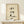 May include: Framed artwork displayed on light wooden shelf showing a cute sitting calico cat with closed eyes and whiskers in watercolor style with black Japanese calligraphy characters above and red seal stamp, rendered on textured beige paper in natural wood frame, small white wrapped gift box with evergreen sprig positioned in front