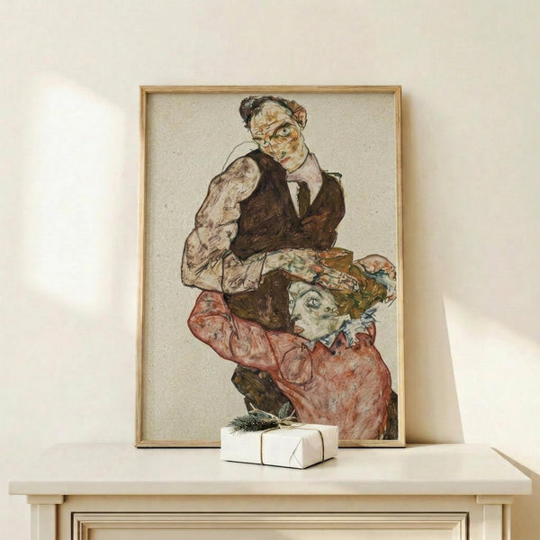 May include: Framed art print displaying an expressionist drawing of two figures in earth tones - a standing man in dark clothing and a kneeling woman in reddish-pink garments. The artwork has a beige background with sketchy, angular lines characteristic of early 20th century style. Shown in thin wooden frame on white shelf next to small wrapped gift with evergreen sprig, against cream wall with soft natural lighting.