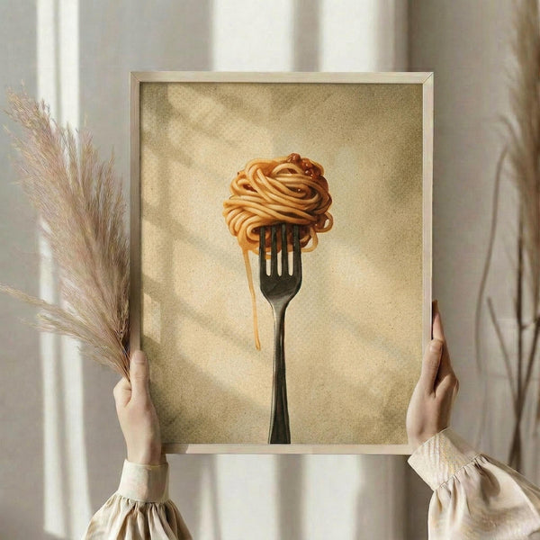 May include: Person in cream sweater holding framed artwork showing pasta twirled on a fork against warm beige textured background, displayed in light wood frame in bright room with dried pampas grass and white curtains