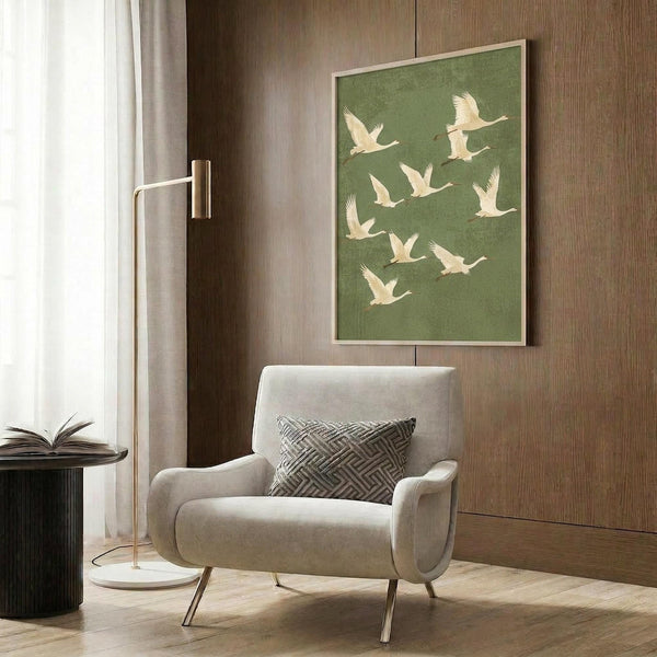 May include: Green wall art print featuring white cranes in flight against sage green background, displayed in modern room setting with beige upholstered armchair, brass floor lamp, and wood paneled wall. Print appears in light wood frame above chair with geometric patterned pillow.