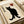 May include: Black cat illustration on aged beige paper with Japanese kanji characters and red heart symbol, displayed in white frame on light wooden surface with white ribbon nearby. The minimalist artwork features a sitting black cat with yellow eyes in traditional Japanese art style.