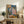 May include: Framed reproduction of Picasso's 1905 painting showing two seated figures - a young person in a diamond-patterned harlequin costume and an adult in a pink shirt. The artwork features muted blues, pinks, and earth tones in Picasso's early period style. Displayed on a rustic wooden sideboard alongside books, a ceramic vase, and potted fern in a modern living room with cream walls and neutral furnishings.