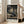 May include: Framed anime poster displayed in bright living room setting with beige couch and large windows. Artwork shows dark-haired samurai character in traditional Japanese room performing sword technique with motion blur effects. Poster features Japanese text at top and bottom, housed in light wood frame, person's hand visible positioning the artwork.
