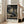 May include: Framed anime poster displaying a samurai character with long dark hair wielding a sword in a traditional Japanese interior. The artwork shows dynamic motion lines around the figure in a wooden room with sliding doors and low table. Japanese text appears at top and bottom of the poster. Person's hand holds the light wood frame against white wall near beige furniture and windows with natural lighting.