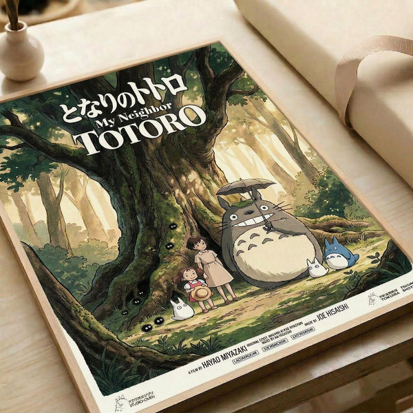 May include: Vintage-style movie poster print featuring animated forest scene with large gray creature holding umbrella, two children, and small white spirits among towering green trees with dappled sunlight. Japanese and English text at top. Print displayed on wooden surface next to white ceramic vase and rolled paper.