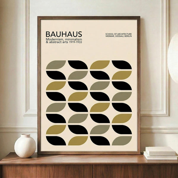 May include: Framed Bauhaus-inspired poster with geometric leaf pattern in black, olive green, and taupe on cream background, displayed on wooden sideboard beside white ceramic vase and stacked books in neutral-toned room with white paneled walls.