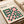May include: Bauhaus modernist poster with geometric pattern of pink squares and green circles arranged in decorative formation on cream background, displayed in light wood frame on neutral surface alongside rolled paper tubes