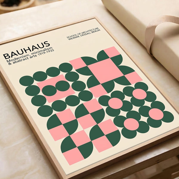 May include: Bauhaus modernist poster with geometric pattern of pink squares and green circles arranged in decorative formation on cream background, displayed in light wood frame on neutral surface alongside rolled paper tubes