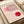 May include: Vintage-style Bauhaus exhibition poster print in wooden frame, featuring geometric design with pink and red circles intersected by curved parallel lines on cream background. Text reads "BAUHAUS" and "Ausstellung Juli - Sept 1923". Frame rests against white fabric with neutral tape roll nearby, showing warm natural lighting and minimalist styling.