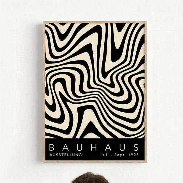 May include: Framed vintage Bauhaus exhibition poster with flowing black and cream wavy stripes creating an optical illusion pattern, mounted in light wood frame on white wall above person with dark hair partially visible at bottom
