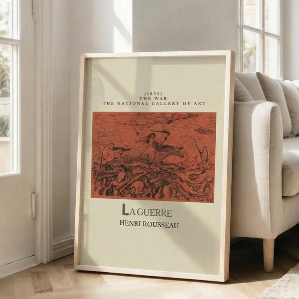 May include: Framed museum-style poster featuring Henri Rousseau's "La Guerre" (1895) from The National Gallery of Art, displayed in bright living room corner next to beige upholstered chair. Print shows red-toned battlefield scene with skeletal remains and dark figure, housed in natural wood frame with cream matting, leaning against white wall near tall windows with natural lighting.