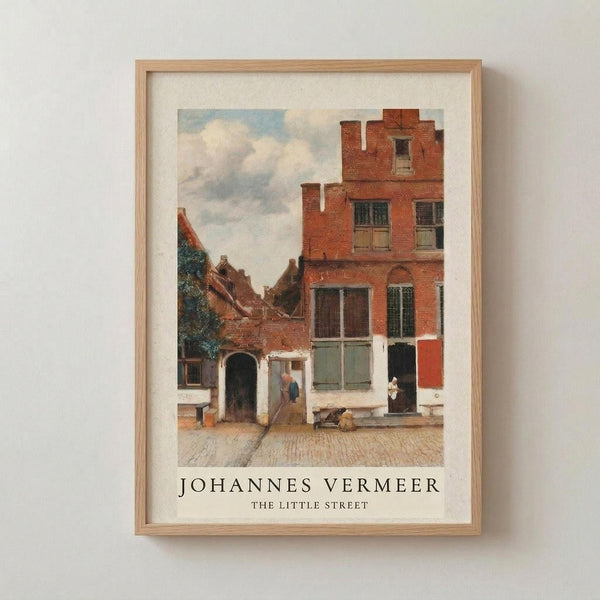 May include: Framed art print of a Dutch Golden Age street scene with red brick buildings, people in a cobblestone courtyard, and cloudy sky. The reproduction features warm earth tones and classical European architecture. Displayed in a light wood frame with white matting against a neutral wall.