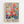 Colorful floral art print in light wood frame hanging on white wall. Vibrant bouquet features pink, coral, yellow and orange flowers with blue and green foliage in painterly style. Bold black "MATISSE" text appears at bottom on cream background. Botanical illustration shows layered blooms, leaves and berries in warm, saturated colors with artistic brushstroke textures.