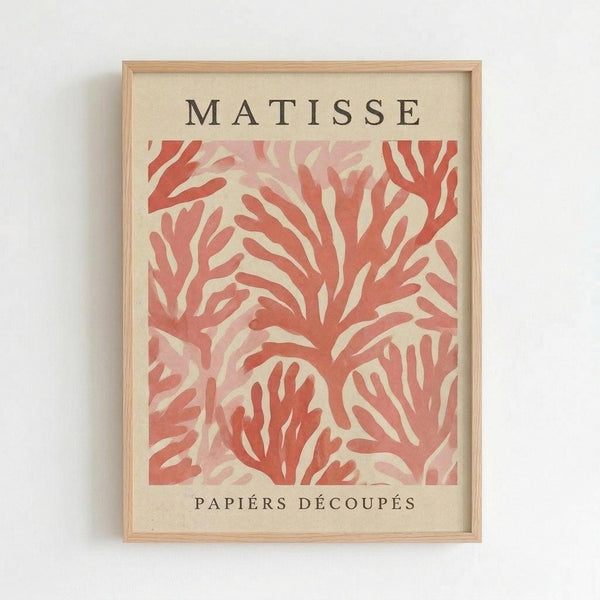 Framed art print featuring abstract coral-colored organic shapes resembling seaweed or foliage against a cream background. The text "MATISSE" appears at the top and "PAPIERS DÉCOUPÉS" at the bottom in dark letters. The artwork is displayed in a light wood frame hanging on a white wall, showing Matisse's signature cut-paper collage style with flowing, curved forms in warm pink and coral tones.