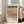 May include: Framed exhibition poster featuring Paul Klee's abstract geometric artwork with earth-toned horizontal bands of triangles, dots, and linear patterns in browns, creams, and dark tones. Light wooden frame leaning against white wall next to beige upholstered sofa in bright, sunlit room with hardwood floors and tall windows.