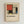 May include: Framed poster print featuring Piet Mondrian's geometric abstract artwork with red, blue, yellow, black and beige rectangular blocks separated by thick black lines. The print includes "PIET MONDRIAN Color Compositions" text and "1921 Te Papa Tongarewa, Exhibition Art" at bottom. Displayed in light wood frame against white textured wall.