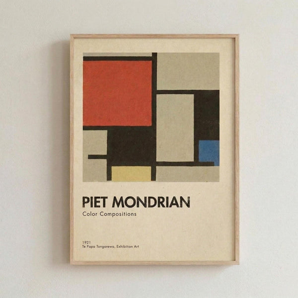 May include: Framed poster print featuring Piet Mondrian's geometric abstract artwork with red, blue, yellow, black and beige rectangular blocks separated by thick black lines. The print includes "PIET MONDRIAN Color Compositions" text and "1921 Te Papa Tongarewa, Exhibition Art" at bottom. Displayed in light wood frame against white textured wall.