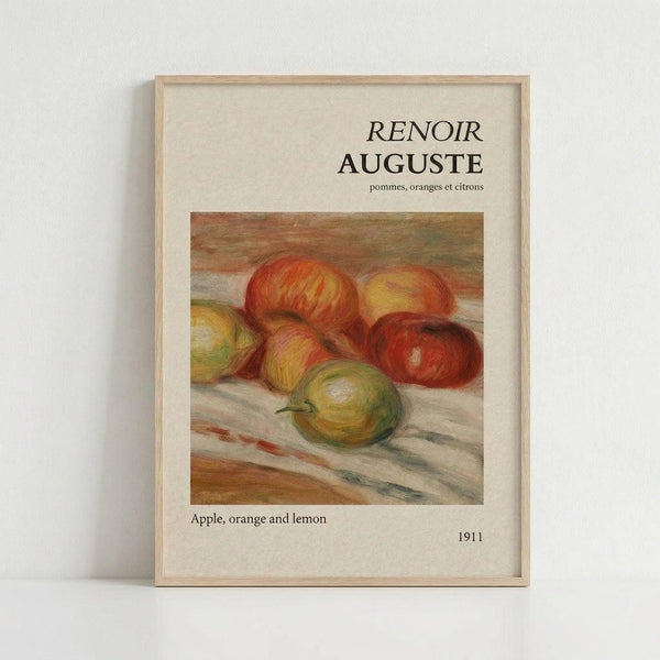 May include: Framed art print featuring Renoir's 1911 still life painting of apples, oranges and a lemon arranged on draped fabric. The artwork shows warm red, orange, yellow and green fruits painted in impressionist style with soft brushstrokes. Text above reads "RENOIR AUGUSTE" with French subtitle, and "Apple, orange and lemon 1911" below. Light wood frame against white wall background.