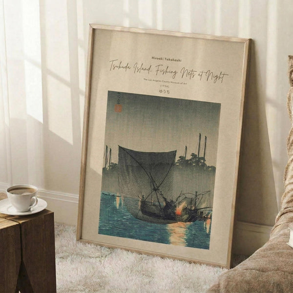 May include: Framed vintage Japanese woodblock print poster showing fishing boats with large nets on teal water at dusk, displayed in light wood frame leaning against white wall corner. Scene includes warm lighting from window, coffee cup on wooden block side table, textured cream rug, and beige upholstered furniture. Print features muted green-gray sky, traditional sailing vessels, and museum exhibition text above artwork.