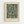 May include: Framed botanical art print in light wood frame hanging on white wall. Features dark green background with cream-colored flowing leaves, branches and small flowers in decorative Arts and Crafts style pattern. Text below reads "William Morris Exhibition Art - Enchanted Blossoms" in serif font on cream matting.