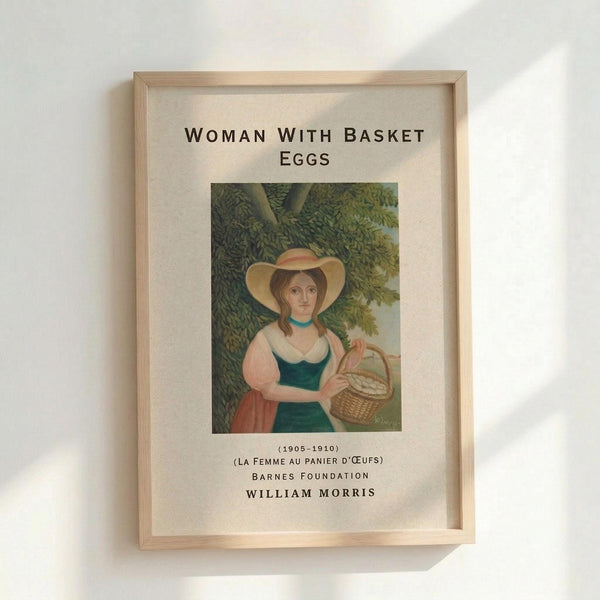 May include: Framed art print showing a woman in period dress with wide-brimmed hat holding a wicker basket of eggs, standing beneath green leafy trees. The vintage-style illustration features soft colors and classic composition. Text above reads "WOMAN WITH BASKET EGGS" with attribution to William Morris and Barnes Foundation below. Natural wood frame against white wall.