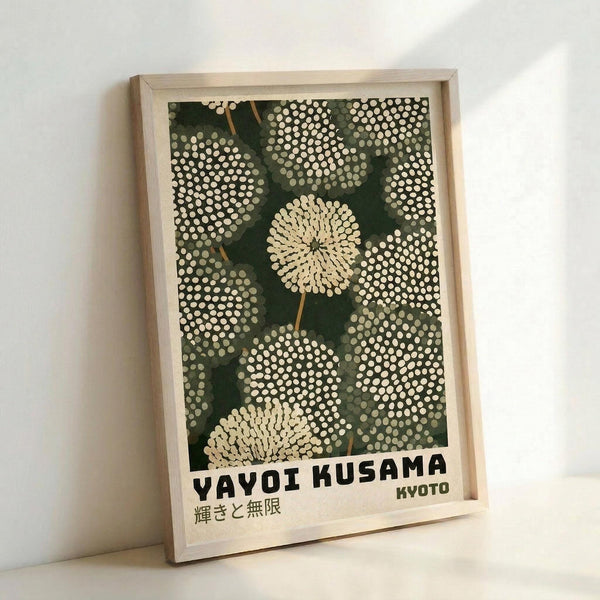 May include: Framed art print leaning against white wall showing stylized dandelion seed heads in cream and white dots on deep green background. Light wood frame contains poster with "YAYOI KUSAMA" and "KYOTO" text at bottom, plus Japanese characters. Polka dot pattern creates organic, flowing shapes reminiscent of botanical illustration with modern artistic style.