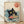 May include: Framed poster print displayed against white wall on wooden floor. Art features black cat with yellow eyes eating ramen from bowl, surrounded by stylized blue ocean waves in traditional Japanese woodblock print style. Noodles hang from cat's mouth, red circular elements visible in bowl and upper corner with Japanese text. Cream background with natural wood frame.
