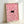 May include: Framed artwork leaning against white wall showing pink and white daisy floral pattern with small black cat silhouette peeking through flowers. Natural wood frame, approximately 12x16 inches, displayed in bright indoor setting with soft lighting and shadows.
