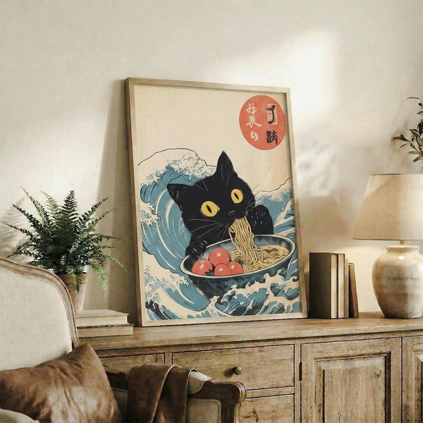 May include: Framed art print featuring a black cat with yellow eyes eating ramen from a white bowl with red garnishes, surrounded by stylized blue ocean waves in traditional Japanese ukiyo-e style. The print has Japanese characters in a red circle and cream background. Displayed on a rustic wooden sideboard next to books, a potted fern, ceramic vase, with a beige armchair visible in a warmly lit living room setting.