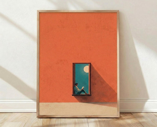 May include: Framed contemporary art print leaning against white wall on light wood floor. Orange and coral geometric background with small figure reading in turquoise doorway or window opening. Cream moon visible in teal sky. Minimalist illustration style with warm sunset colors and architectural shadow. Natural wood frame with clean lines.