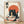 Framed poster featuring a black cat with white eyes eating ramen noodles with chopsticks, set against a large orange sun. The cat sits beside a decorative bowl filled with noodles, egg, and garnishes, with additional small bowls and a bottle nearby. Japanese text appears in the corners. The artwork uses a vintage Japanese woodblock print style with muted colors on cream background. The wooden frame leans against a white wall on light wood flooring.