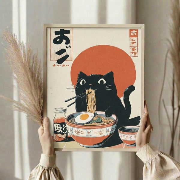 May include: Hands holding a framed poster featuring a black cat with large white eyes eating ramen noodles with chopsticks, orange sun backdrop, Japanese text, vintage ukiyo-e art style in orange and cream colors. Person wears beige ruffled sleeves, dried pampas grass visible beside light wooden frame against neutral curtained background.