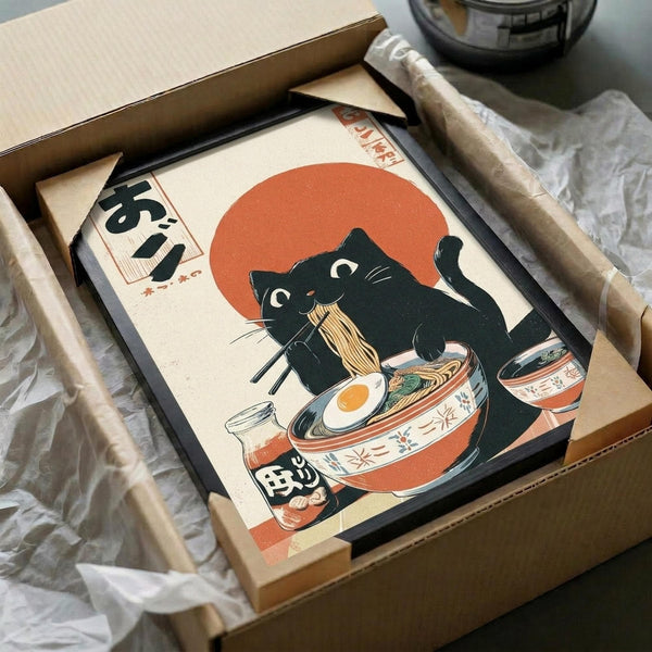 May include: Framed Japanese-style artwork featuring a black cat with white chest markings eating ramen noodles from a decorative bowl, set against an orange sun background. The print shows ukiyo-e artistic style with Japanese characters visible. Frame appears dark-colored, displayed in shipping box with brown paper wrapping materials on white tissue paper.