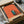 May include: Framed art print being carefully unpacked from cardboard shipping box with protective tissue paper. The contemporary artwork features a minimalist orange background with a geometric doorway or window opening revealing a teal interior scene with a figure reading beneath a crescent moon. The piece has clean lines and modern color blocking in warm coral and cool turquoise tones, shown in a simple black frame.
