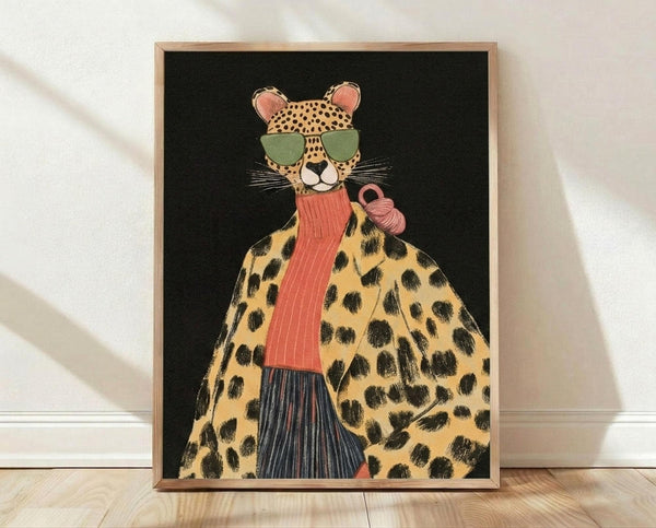 May include: Framed art print leaning against white wall on light wood floor. Black background artwork shows anthropomorphic cheetah wearing green sunglasses, coral knit scarf, leopard print coat with black spots, and dark striped skirt. Pink coffee cup held in hand. Natural wood frame, soft lighting creates diagonal shadows across white textured wall.