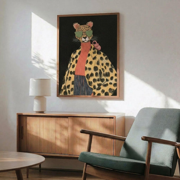 May include: Framed artwork on white wall showing stylized leopard wearing green sunglasses, coral scarf, and spotted coat against dark green background. Modern mid-century living room with sage green upholstered chair, wooden sideboard, small table lamp with white shade. Warm natural lighting creates geometric shadows across the minimalist space.