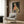 May include: Stylized cheetah wearing green sunglasses, coral scarf, and leopard print coat displayed in framed artwork on wood-paneled wall above beige upholstered chair with geometric pillow, gold floor lamp, and dark round side table with open book in modern living room setting