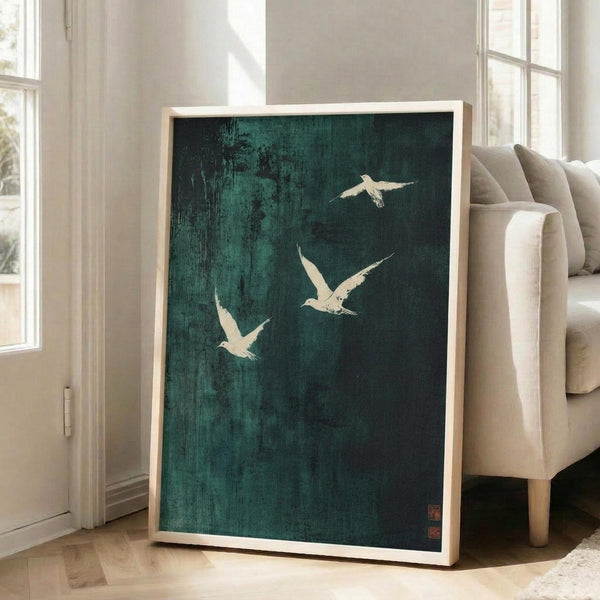 May include: Large framed art print with deep teal-green textured background featuring three white birds in flight, displayed in light wood frame leaning against white wall next to beige upholstered chair in bright, minimalist living room with tall windows and hardwood floors.