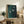 May include: Framed artwork with dark teal background featuring three white birds in flight, displayed on rustic wooden sideboard alongside fern plant, ceramic vase, and stacked books in warm-toned living room setting