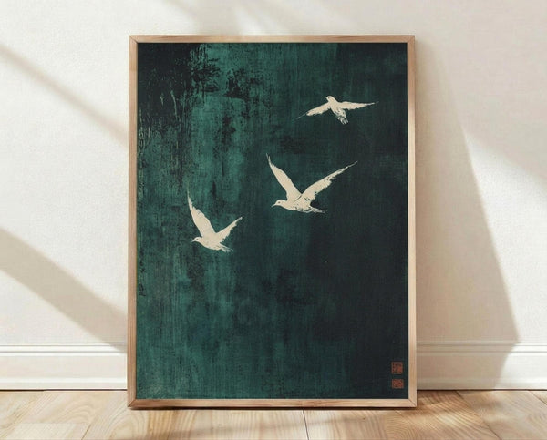May include: Framed artwork showing three white birds in flight against a dark teal-green textured background with brushstroke effects, displayed in a light wood frame leaning against a white wall on wooden flooring with natural lighting creating soft shadows