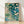 Impressionist watercolor framed poster depicting cream wildflowers blooming along a tranquil stream with lily pads, rendered in soft teal, pale pink, and sage green tones creating a serene, dreamy garden scene.