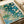 Soft impressionist watercolor poster art featuring cream-colored blooms and aquatic florals in shades of teal, pale yellow, and sage, capturing the peaceful essence of a misty garden stream.