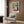 Framed wall poster of a luminous Mediterranean room interior with green plants, doors opening to light, and a calming palette of terracotta, blue, and cream in modern impressionist style.