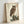 Wall-mounted poster of a Japanese woodblock owl composition showing the bird in a natural setting with reeds and rocky terrain, executed in warm creams and dark browns with fine detail work.