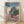 Serene Japanese woodblock-style poster of Nagoya Castle surrounded by pale pink cherry blossoms and forest green trees, rendered in soft cream and gold tones.