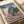 Japanese vintage woodblock art print of a castle landscape with cherry blossoms, stone walls, and forest green trees in soft blue, pink, and cream tones.