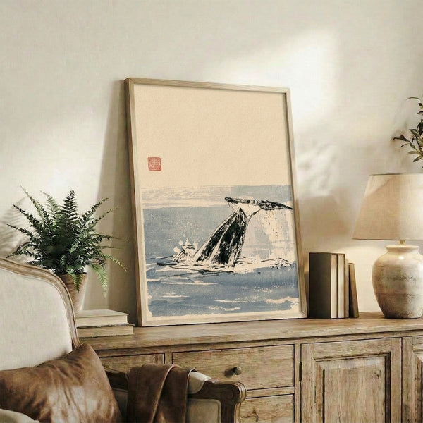 Serene seascape in sumi-e style showing a whale tail breaking through blue-gray waters with minimal black brushwork and white negative space, framed on wall.