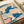 Framed crane wall art in the Japanese woodblock tradition, with the bird gracefully positioned among cloud motifs in deep blue, coral, and gold pigments on cream background.